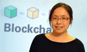 Hong Wan standing in front of a screen displaying the word "Blockchain"